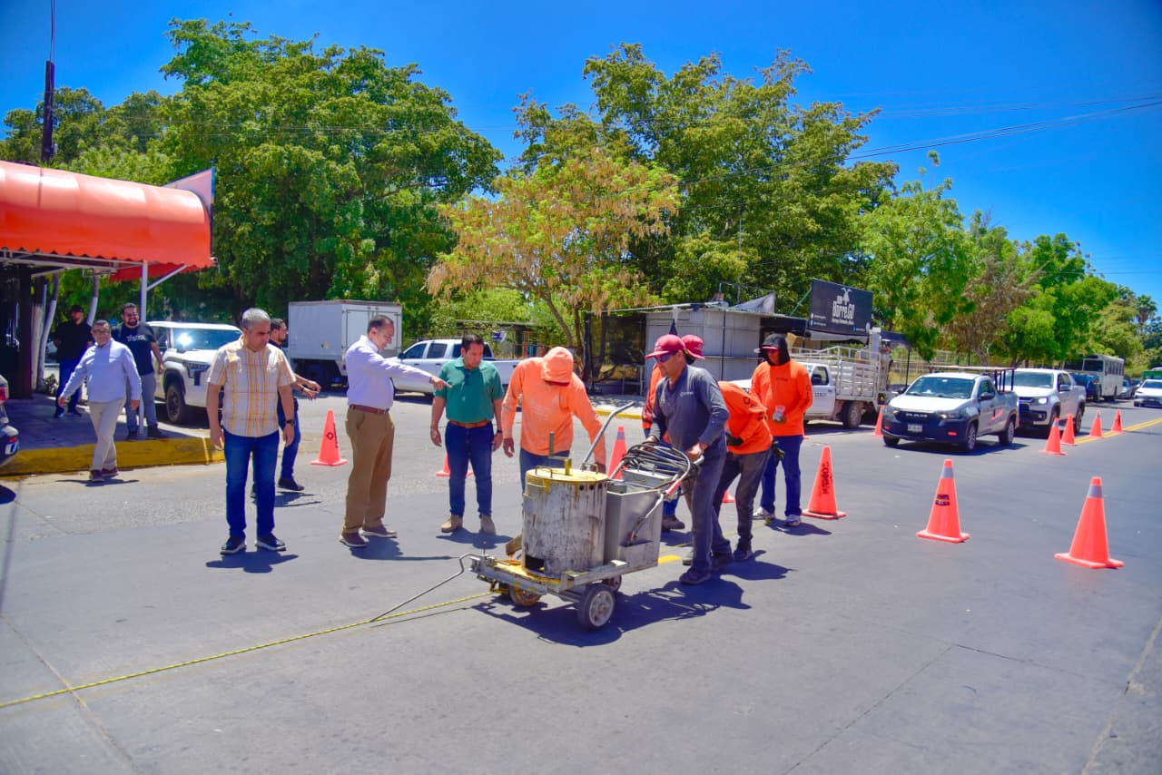 Conos de precaución color naranja junto a personas trabajando pintando color amarilla
