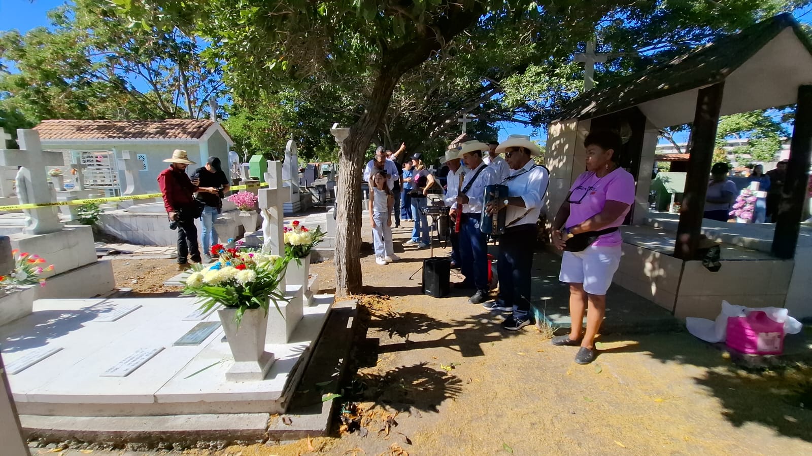 Personas en panteón con flores e instrumentos musicales