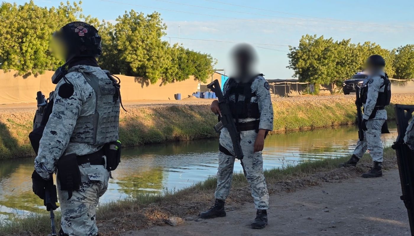 Tres elementos de la Guardia Nacional con armas y una patrulla detrás de ellos