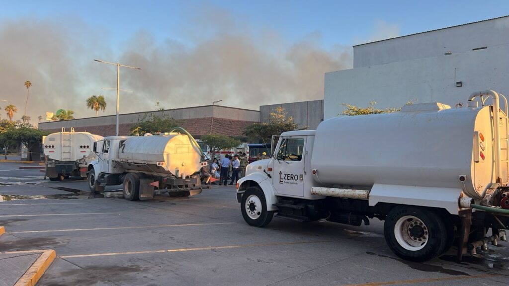 Pipas con agua en un estacionamiento con humo al fondo