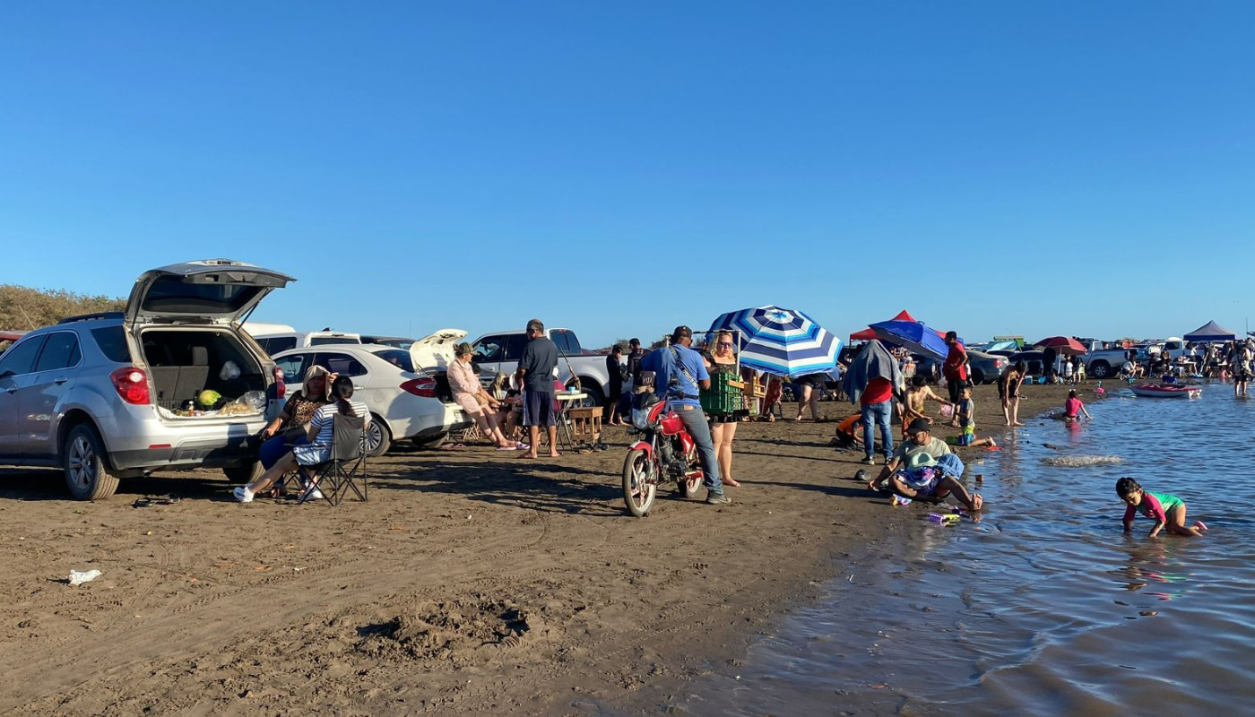 Personas en carros y palapas en la orilla de una playa