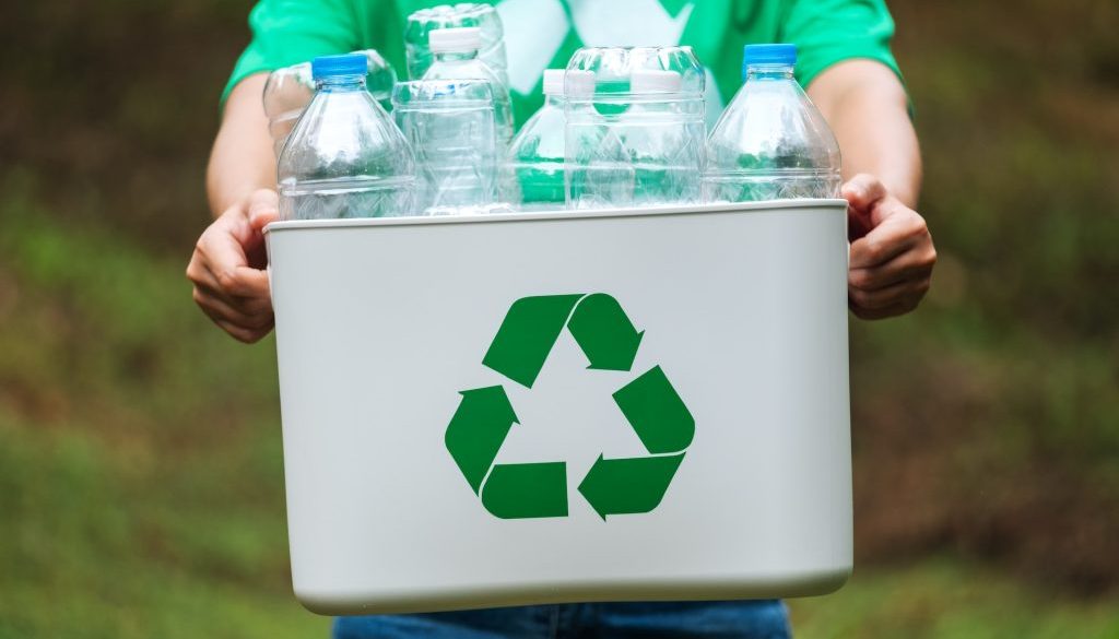 Persona cargando una caja con botellas de plástico.
