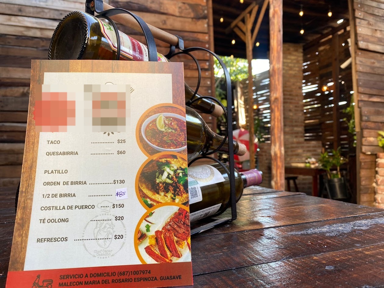 Carta de menú de restaurante en mesa con botellas de vino detrás