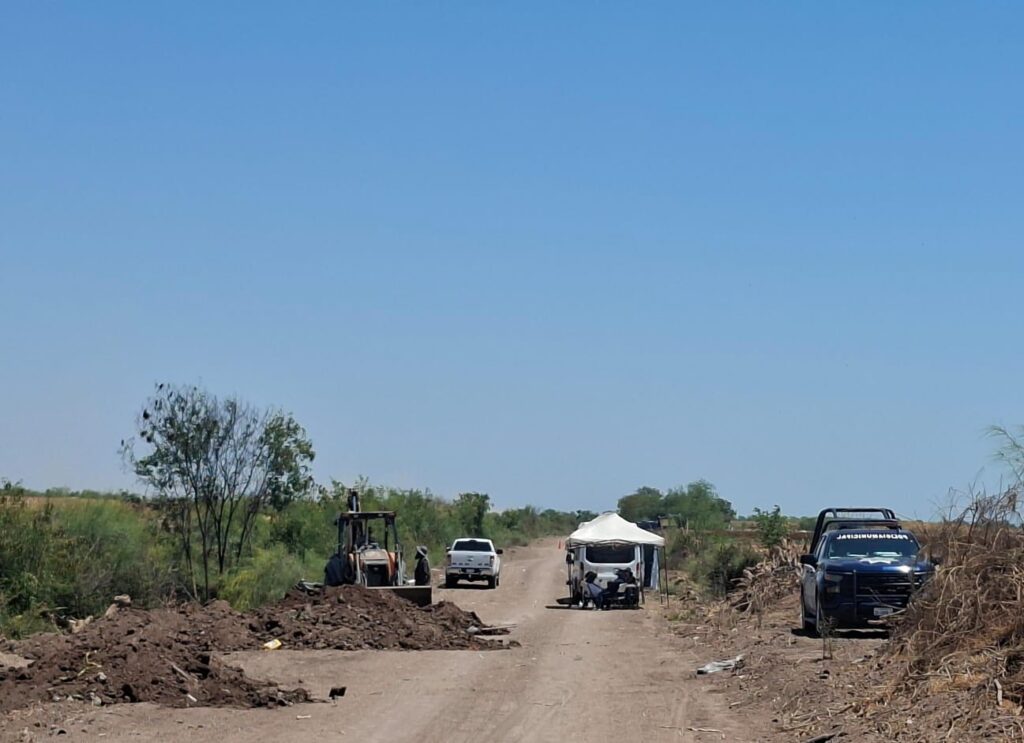 Terreno de terracería junto a unidades de la policía y carpas blancas