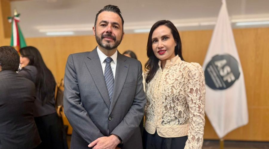 dos personas de frente y al fondo una bandera blanca con un logo en el medio