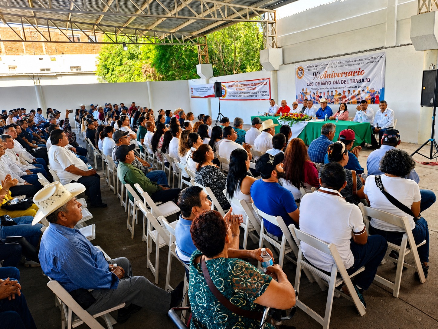 Personas sentadas bajo una techumbre en un evento de conmemoración del Día del Trabajo en Guasave