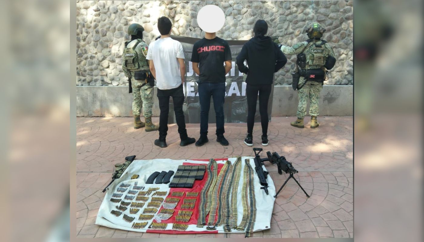 Militares sosteniendo una lona, delante tres sujetos, dos de espaldas y uno de frente con el rostro cubierto y en el suelo una lona con objetos y armas