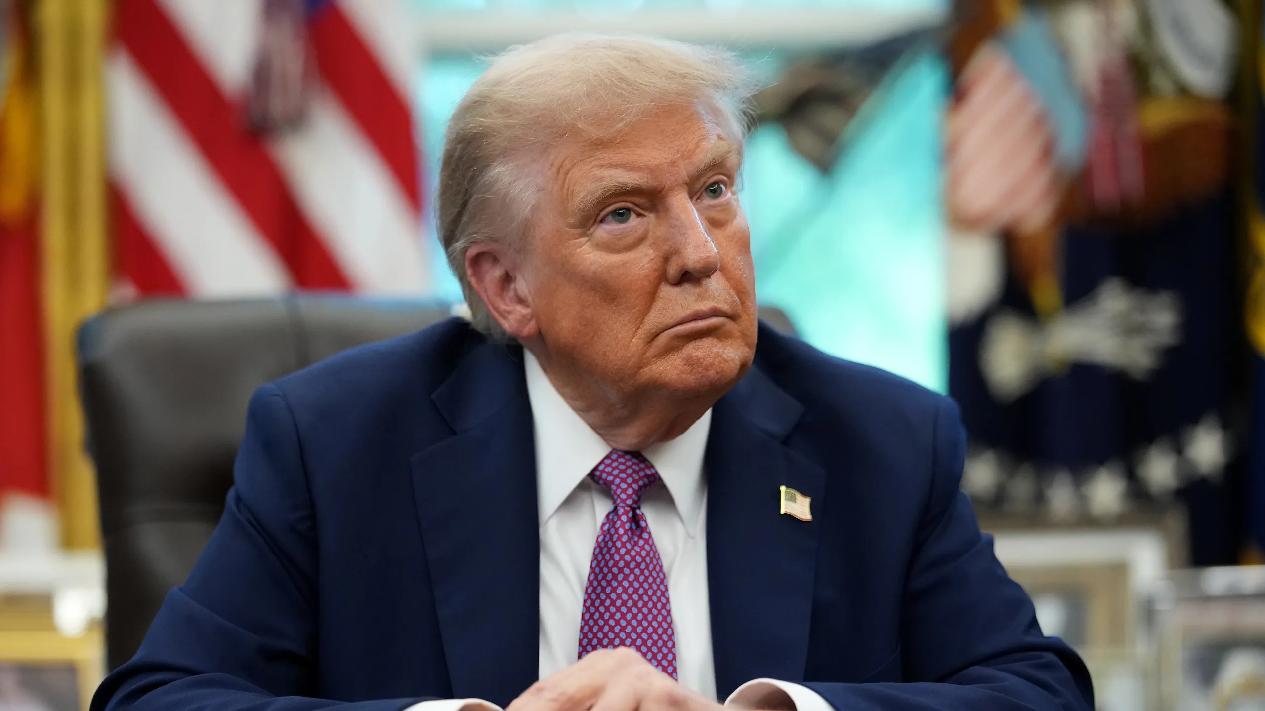 Donald Trump sentado en su oficina en la Casa Blanca con banderas