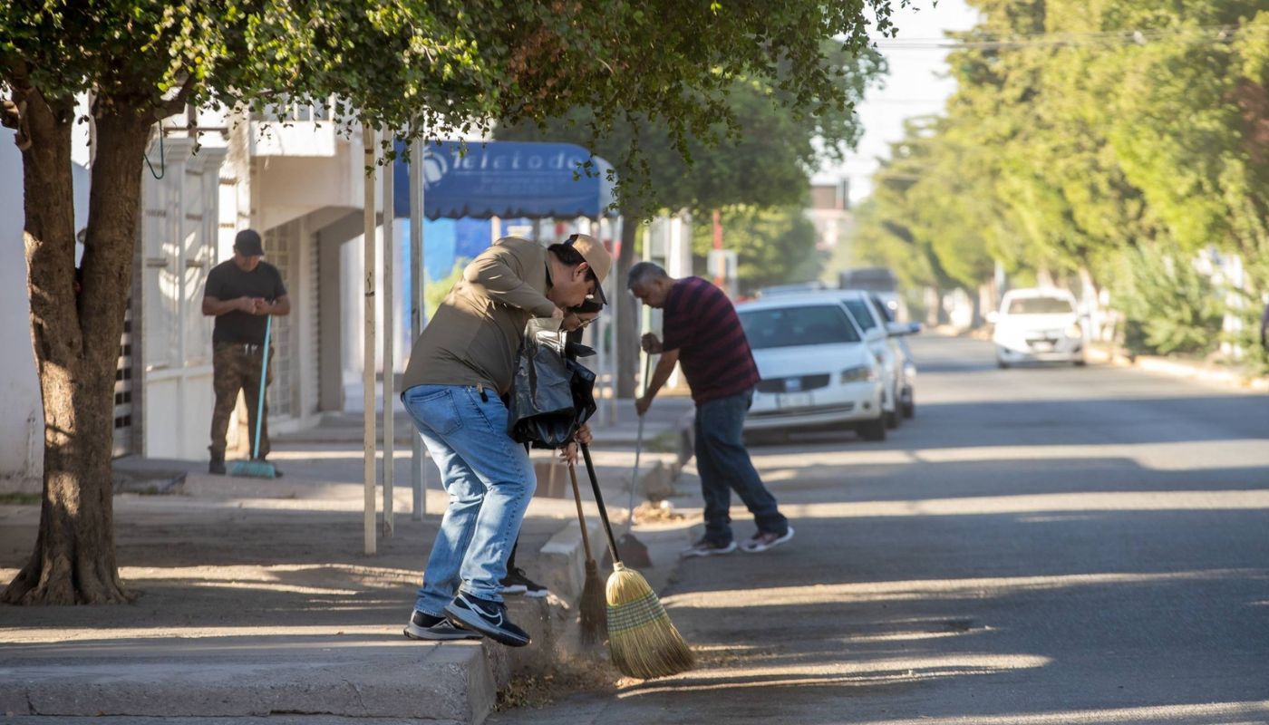 Personas barriendo en una calle y carros al fondo