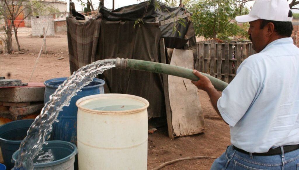Persona con una manguera vertiendo agua en contenedores