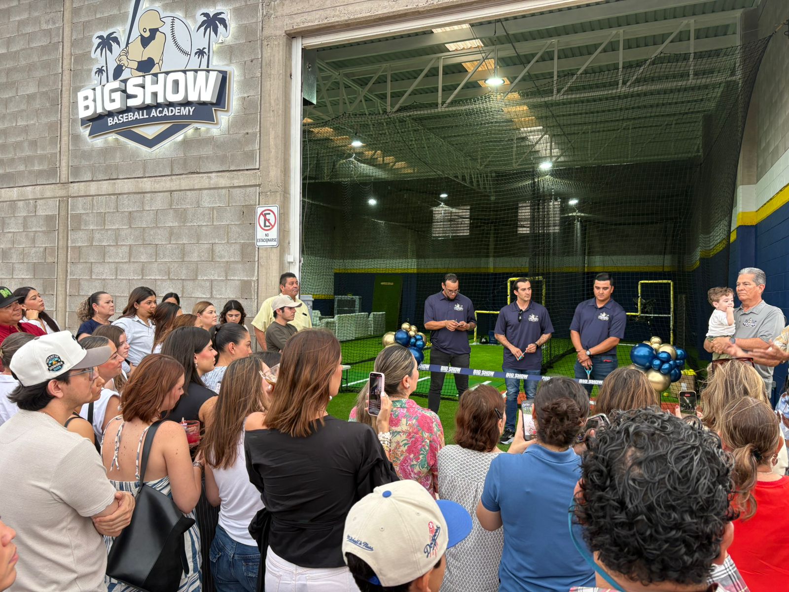 Personas en inauguración de una academia de beisbol con globos azules