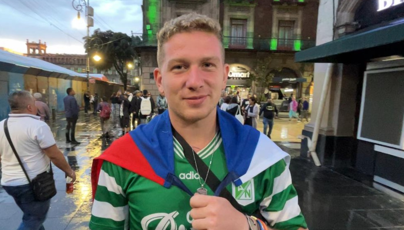 Daniel Hruby, influencer checo, con un jersey deportivo y una bandera en su espalda, en una calle y al fondo muchas personas