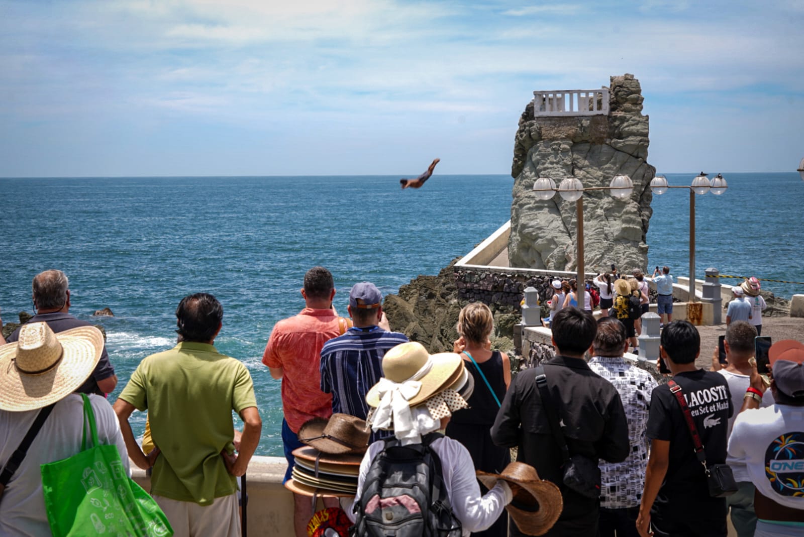 Turistas de espectadores de un clavadista en playa de Mazatlán