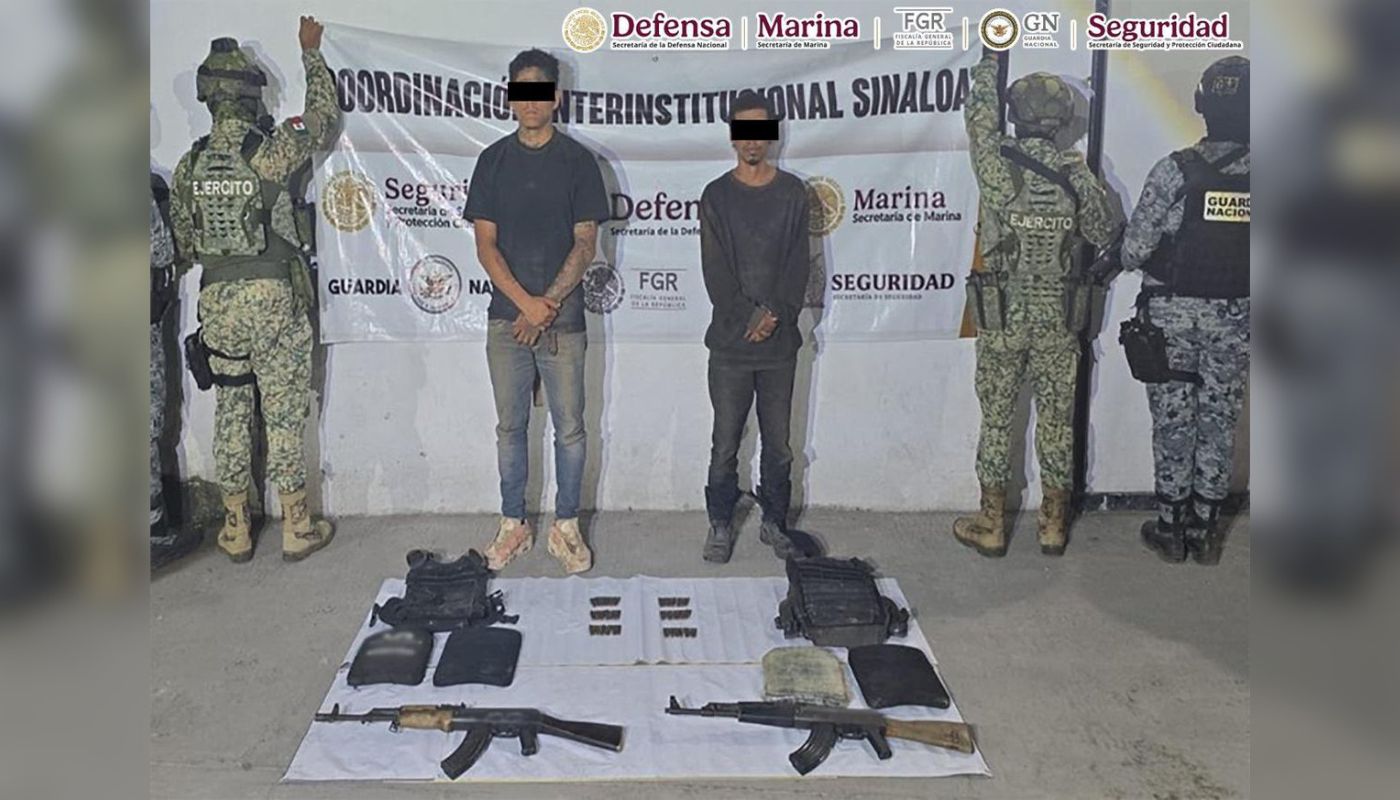Dos personas con el rostro cubierto y las manos esposadas al frente, mientras agentes de seguridad sostienen una lona y en el piso armas y objetos