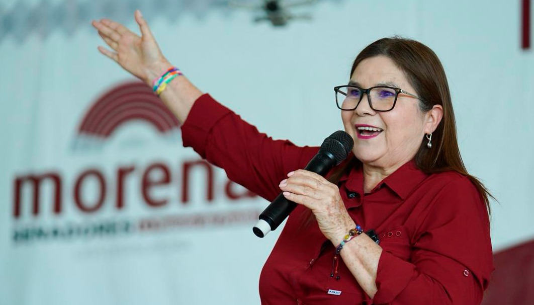 Imelda Castro con la mano arriba y el logo de Morena atras