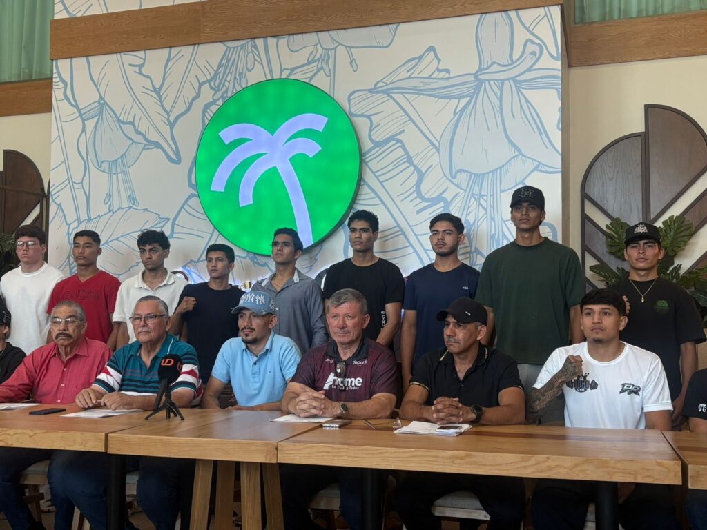 Boxeadores parados y directivos sentados con una mesa y micrófono