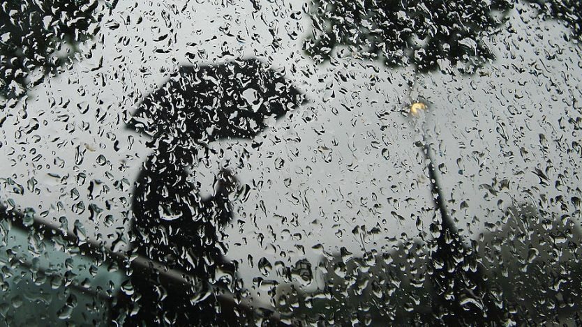 Gotas de lluvia y el reflejo de una persona con paraguas.