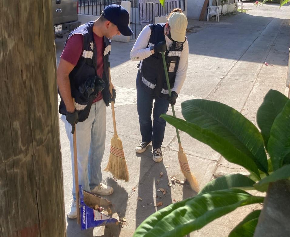 Dos personas con escobas en la calle y un recogedor
