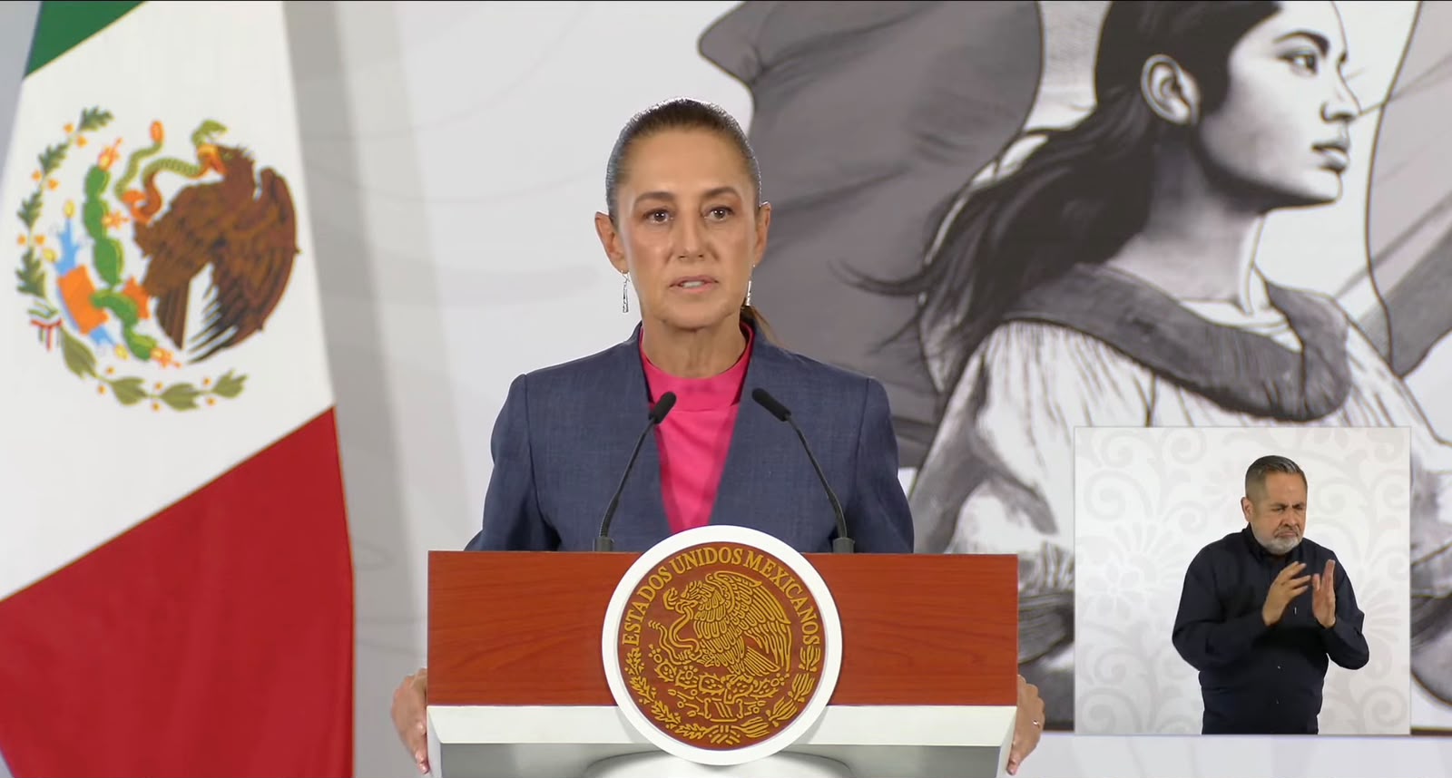 Claudia Sheinbaum con saco azul y blusa rosa y una bandera de México
