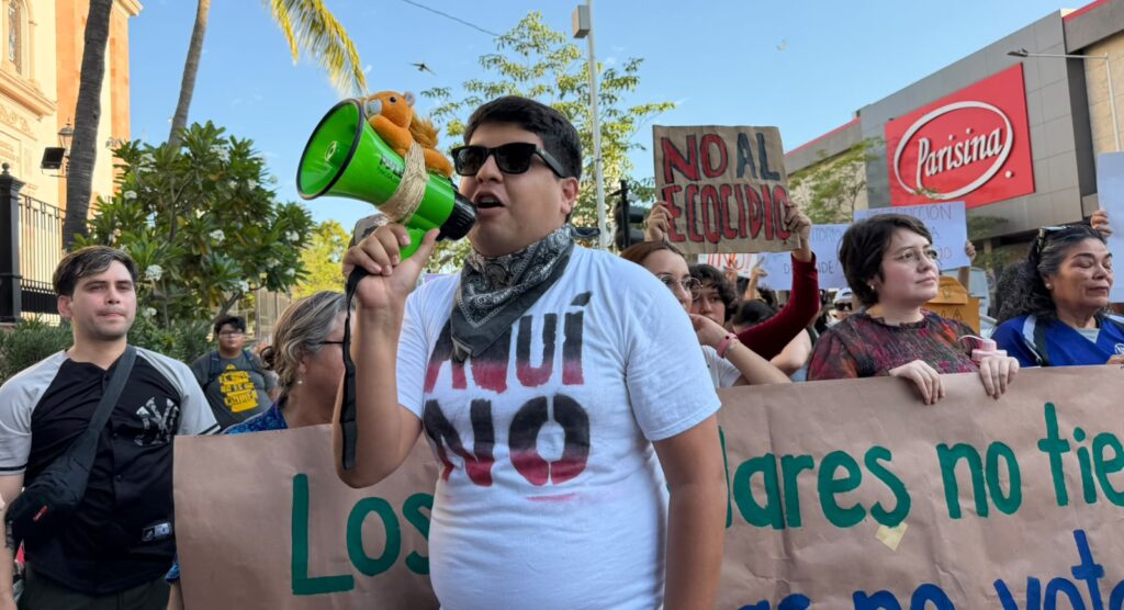 Persona con un megafono y playera de Aquí No
