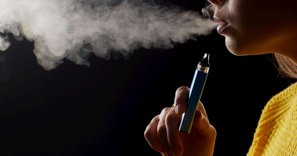 Mujer joven fumando vapeador con fondo negro