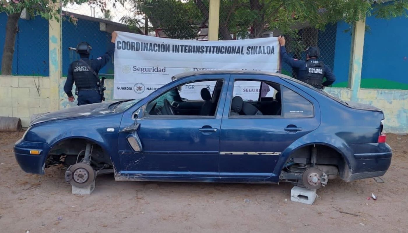 Carro sin llantas sobre blocks de cemento y dos elementos de seguridad con una lona