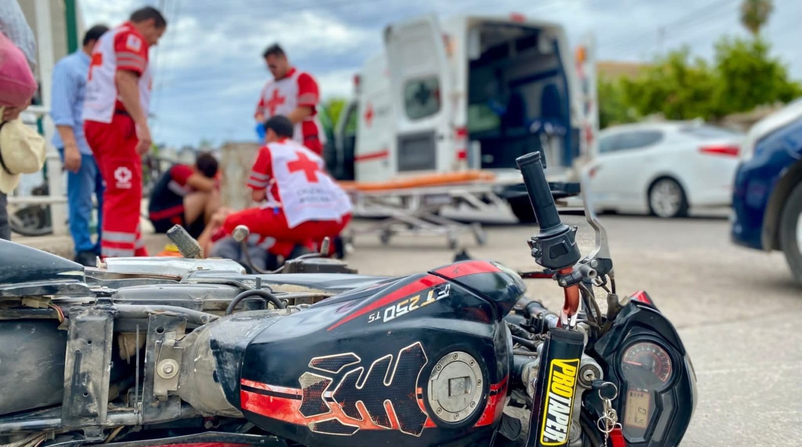 Motocicleta tirada en una calle y al fondo personal de Cruz Roja