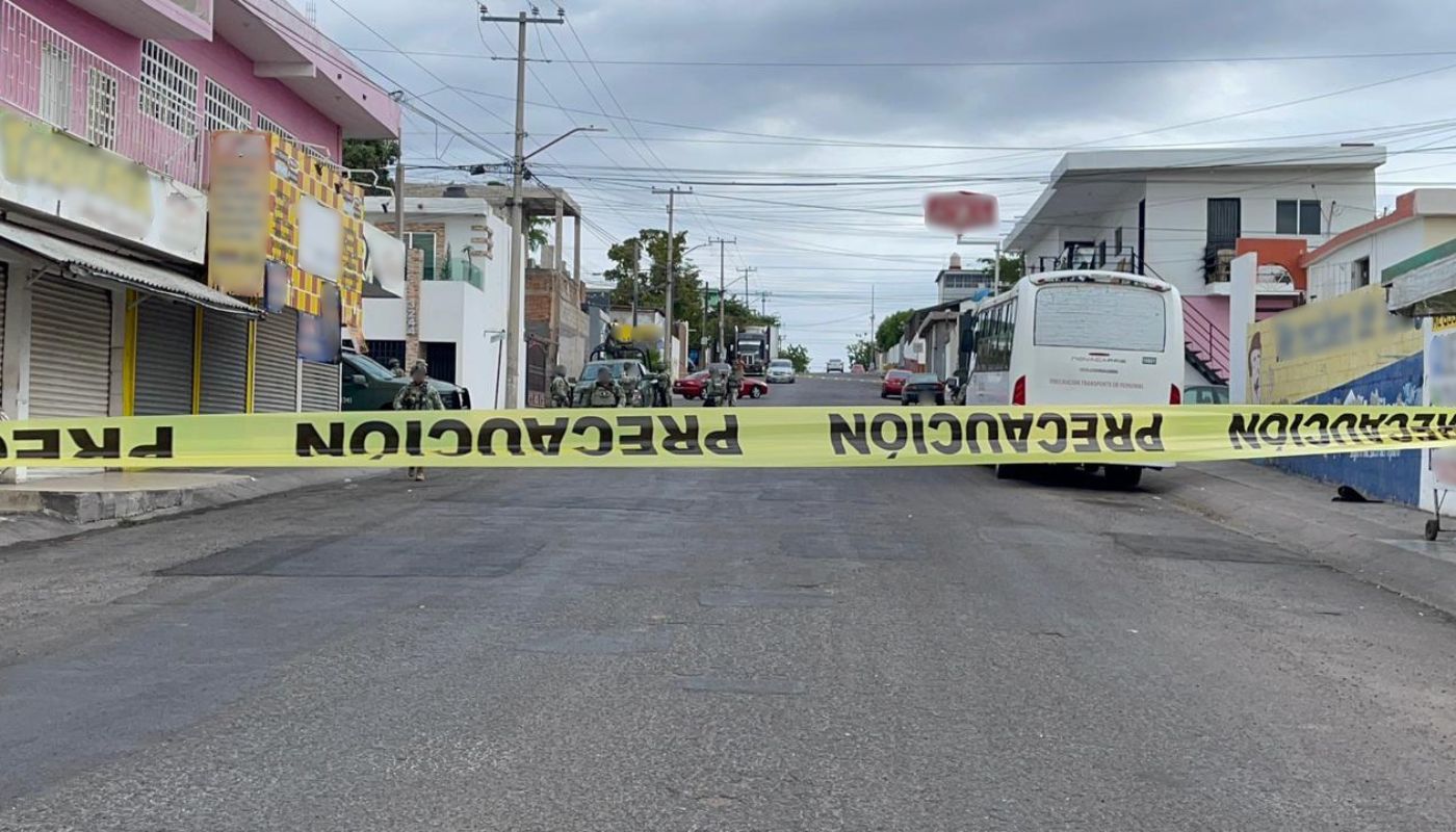 Cinta amarilla de precaución en una calle donde hay una unidad militar y elementos desplegados por la zona, se observan carros y unidades de carga estacionados