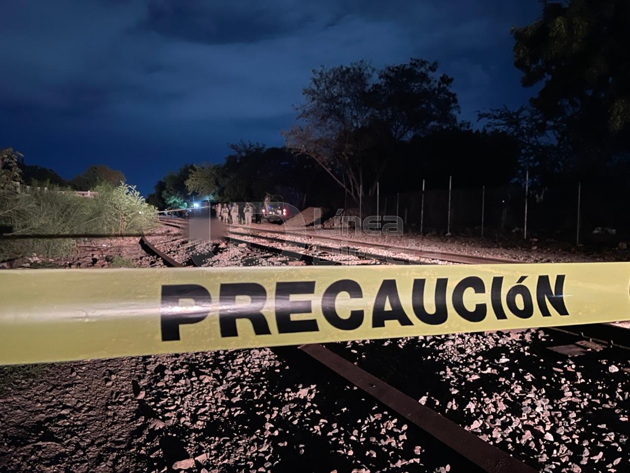 cinta amarilla de precaución sobre unas vías del tren y al fondo elementos militares
