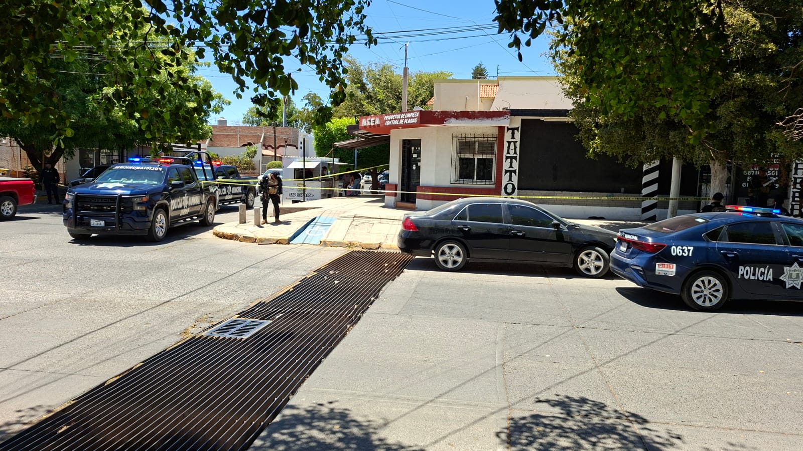 Patrullas y unidades policiacas en una calle junto a un establecimiento con una cinta de precaución