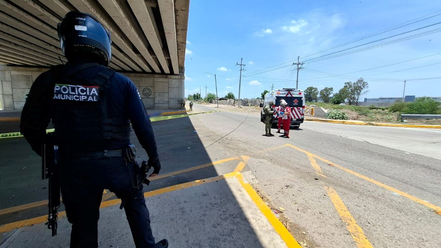 Elementos policiacos y de la Cruz Roja junto a una carretera bajo un puente con una cinta de precaución