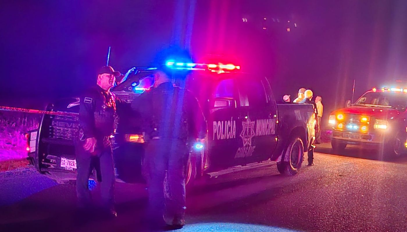 Unidad policiaca y dos elementos parados junto a ella, en una calle de noche