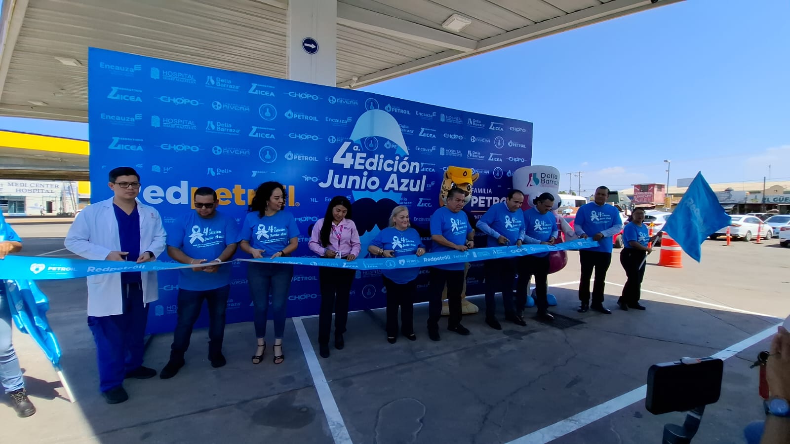 Personas con playera azul y fondo azul con marcas y un listón