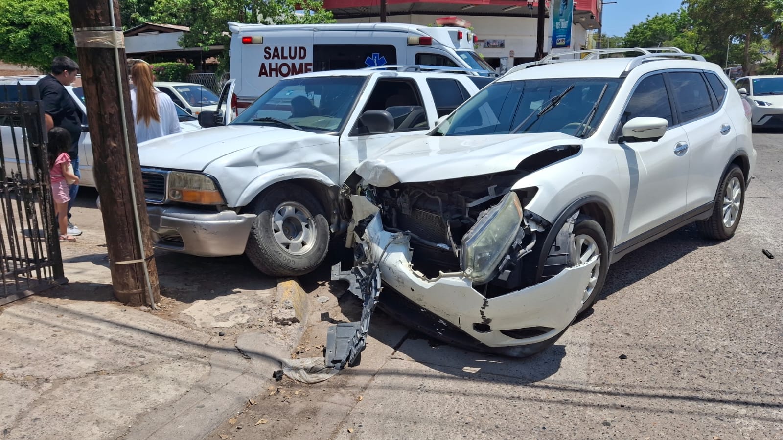 Dos camionetas de color blanco impactadas y sobre la banqueta luego de un choque tipo carambola, al fondo se observa una unidad de emergencias