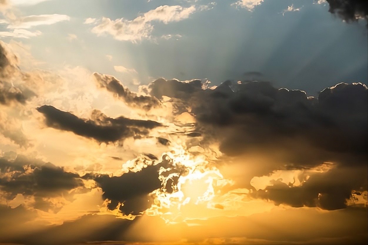Cielo azul con nubes y sol resplandesciente saliendo con rayos entre la nubosidad