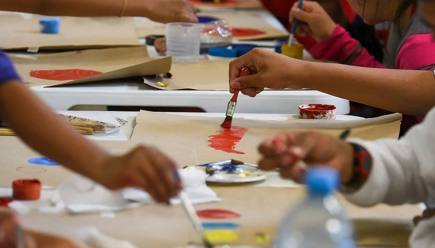 Manos de niños pintando con pinceles y pintura sobre una lona