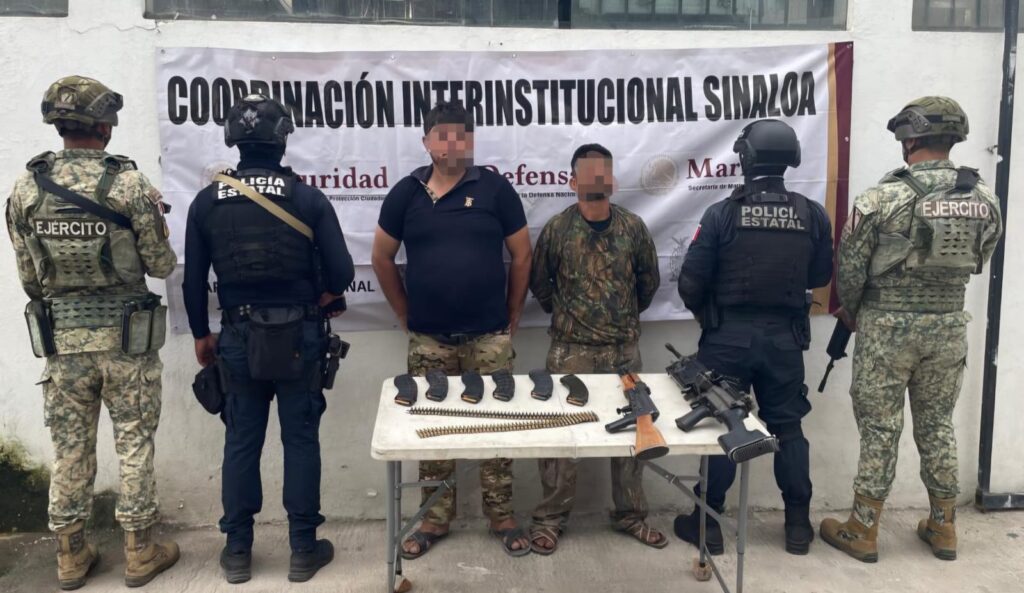 Elementos policiacos de espaldas y dos civiles al centro con el rostro cubierto y las manos esposadas