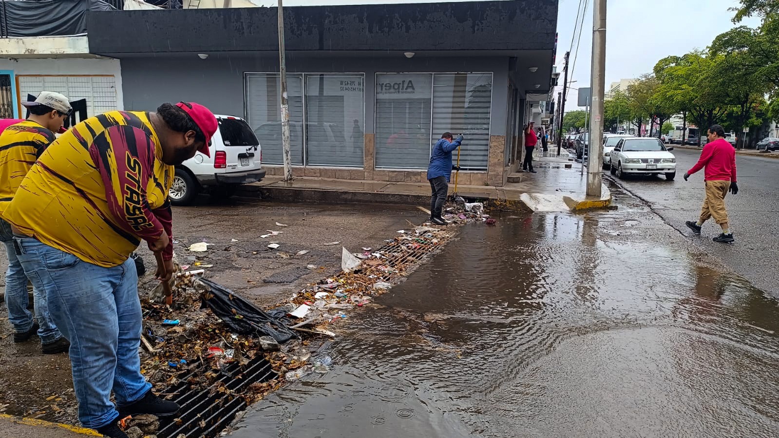 Cuadrilla de limpieza con playera amarilla y alcantarilla con basura