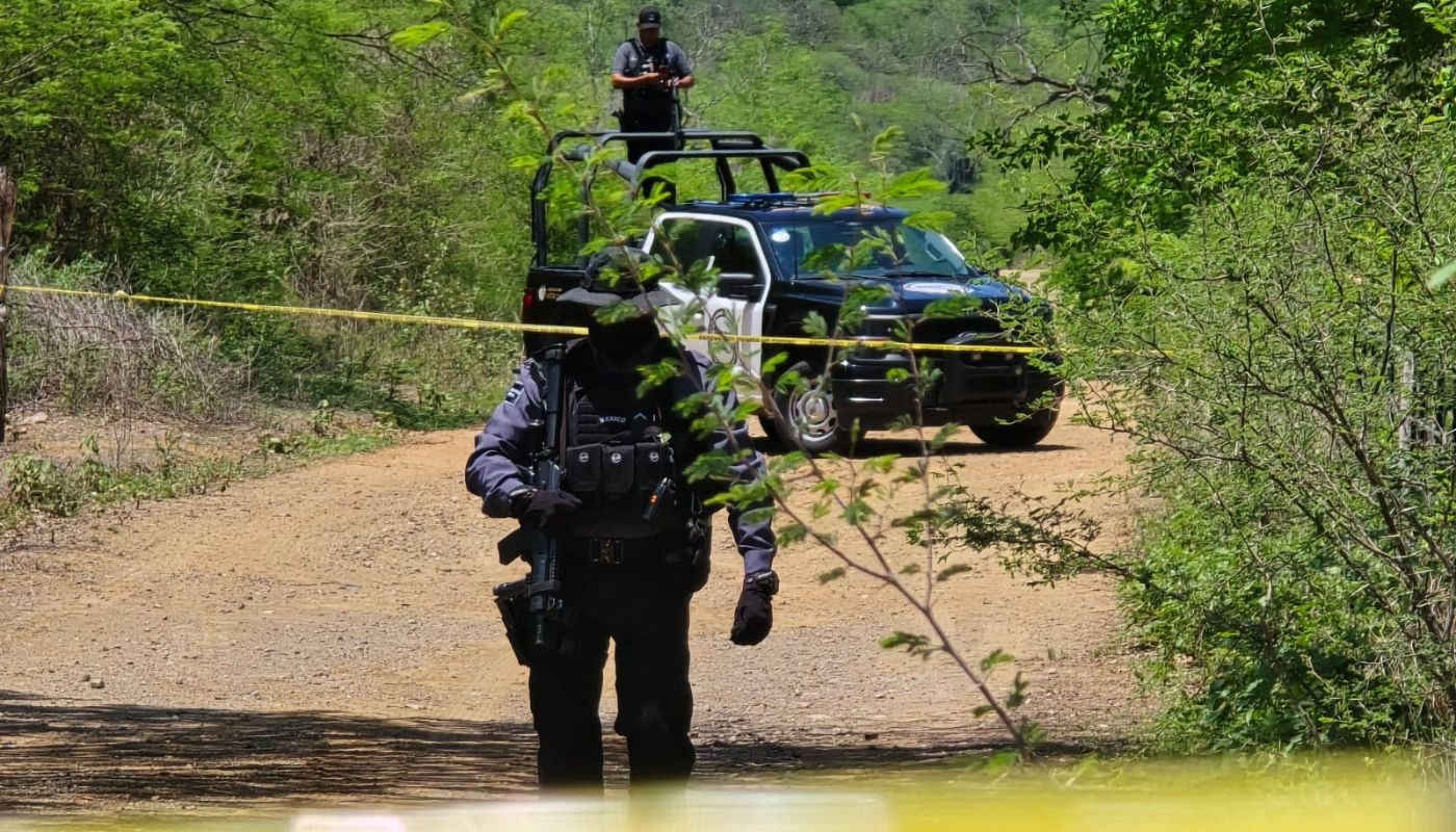 Personal policiaco y una patrulla en un camino de terracería en una zona tipo sierra y una cinta de precaución