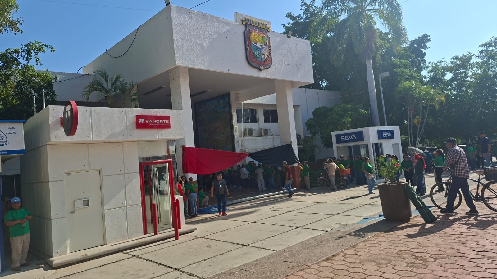 personas manifestandose afuera del Ayuntamiento de Guasave con una bandera rojinegra