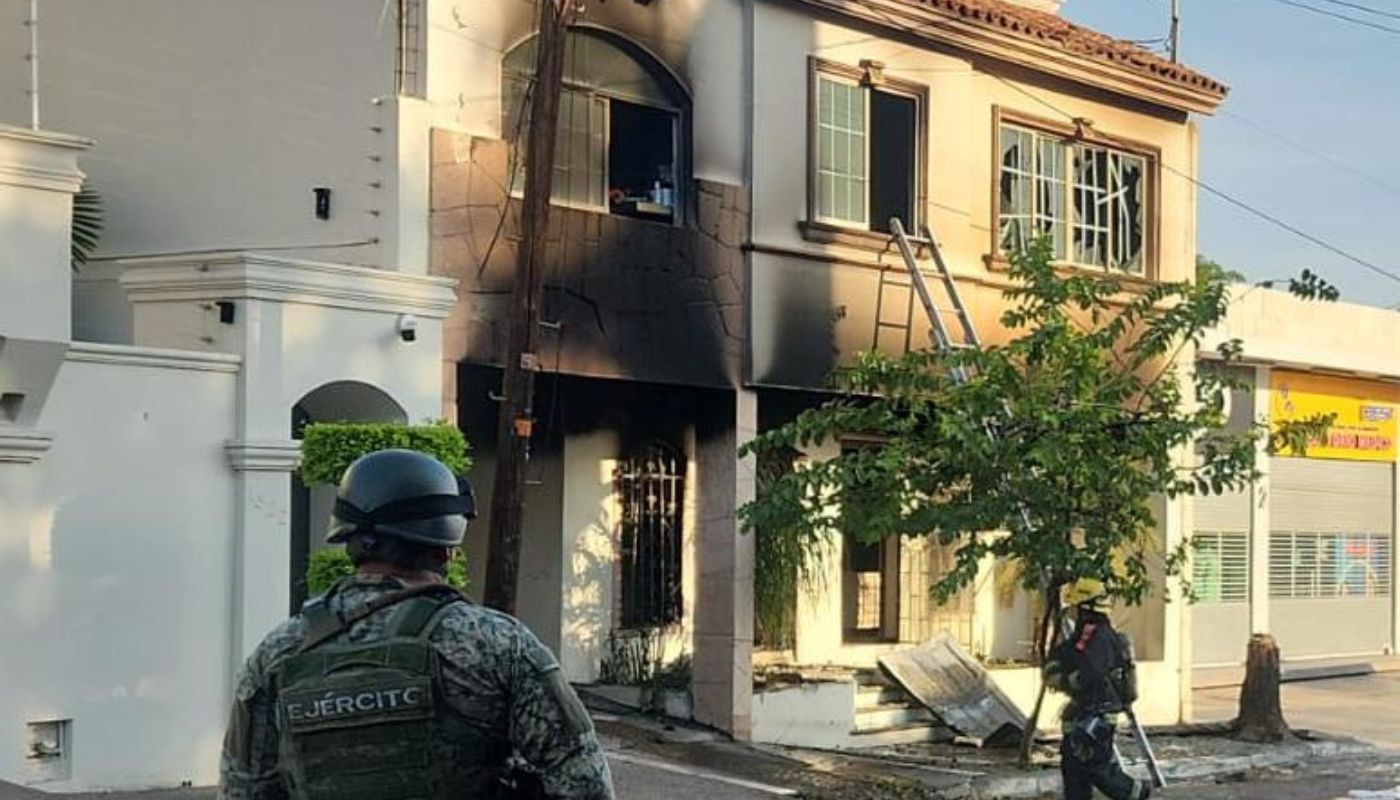 Elemento militar de espaldas frente a una casa con manchas de humo tras incendio