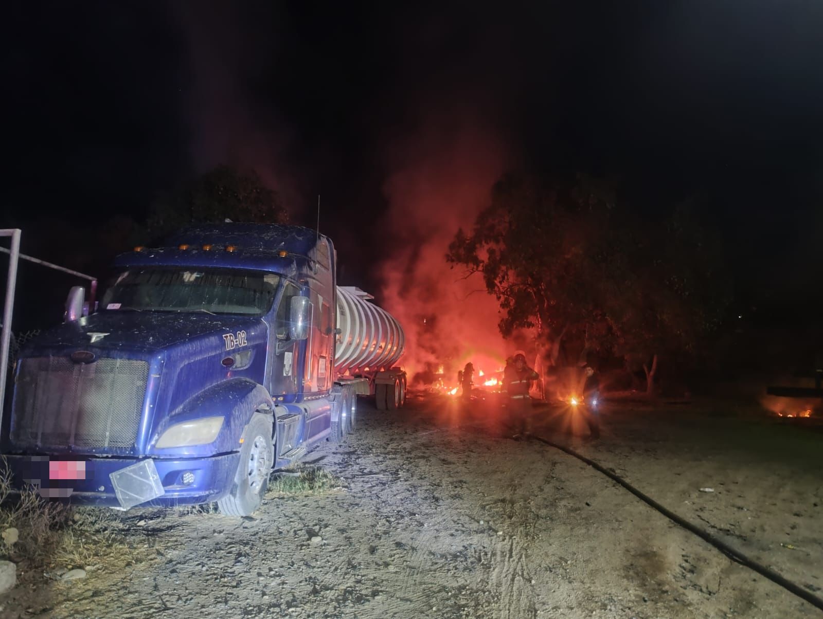 Tráier estacionado y al fondo llamas y humas por el incendio
