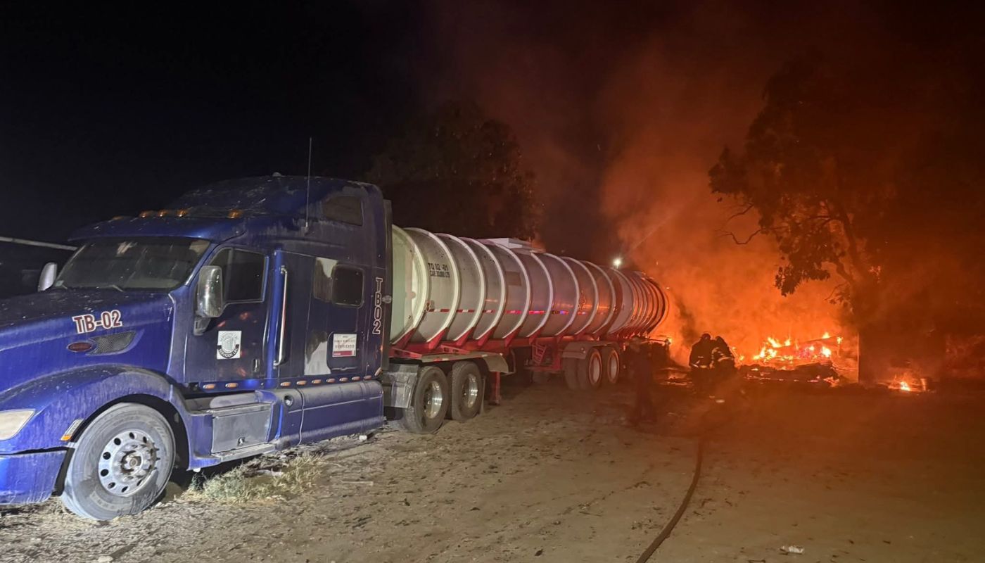 Tráier estacionado y al fondo llamas y humas por el incendio