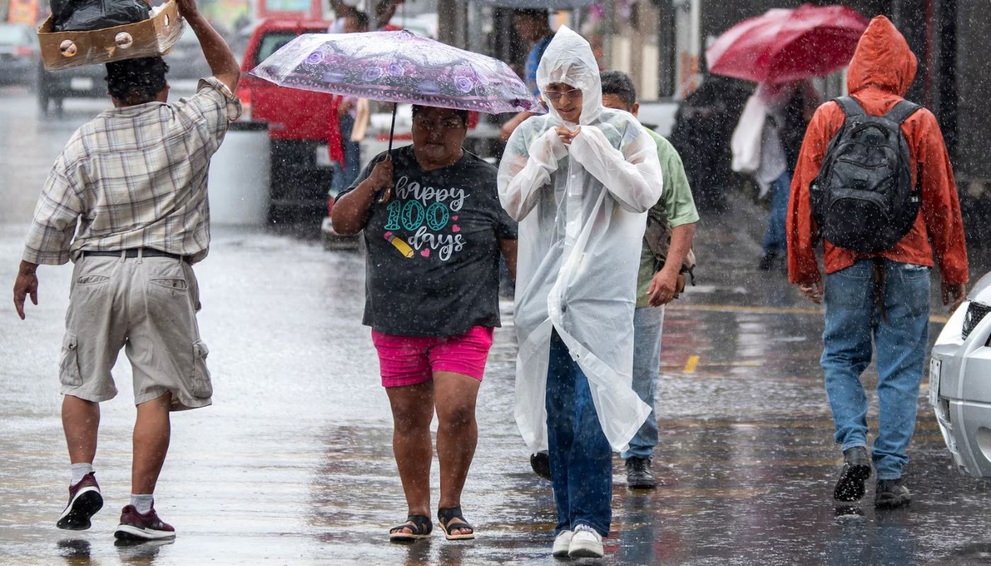 personas con paraguas e impermeables caminando en una calle bajo la lluvia