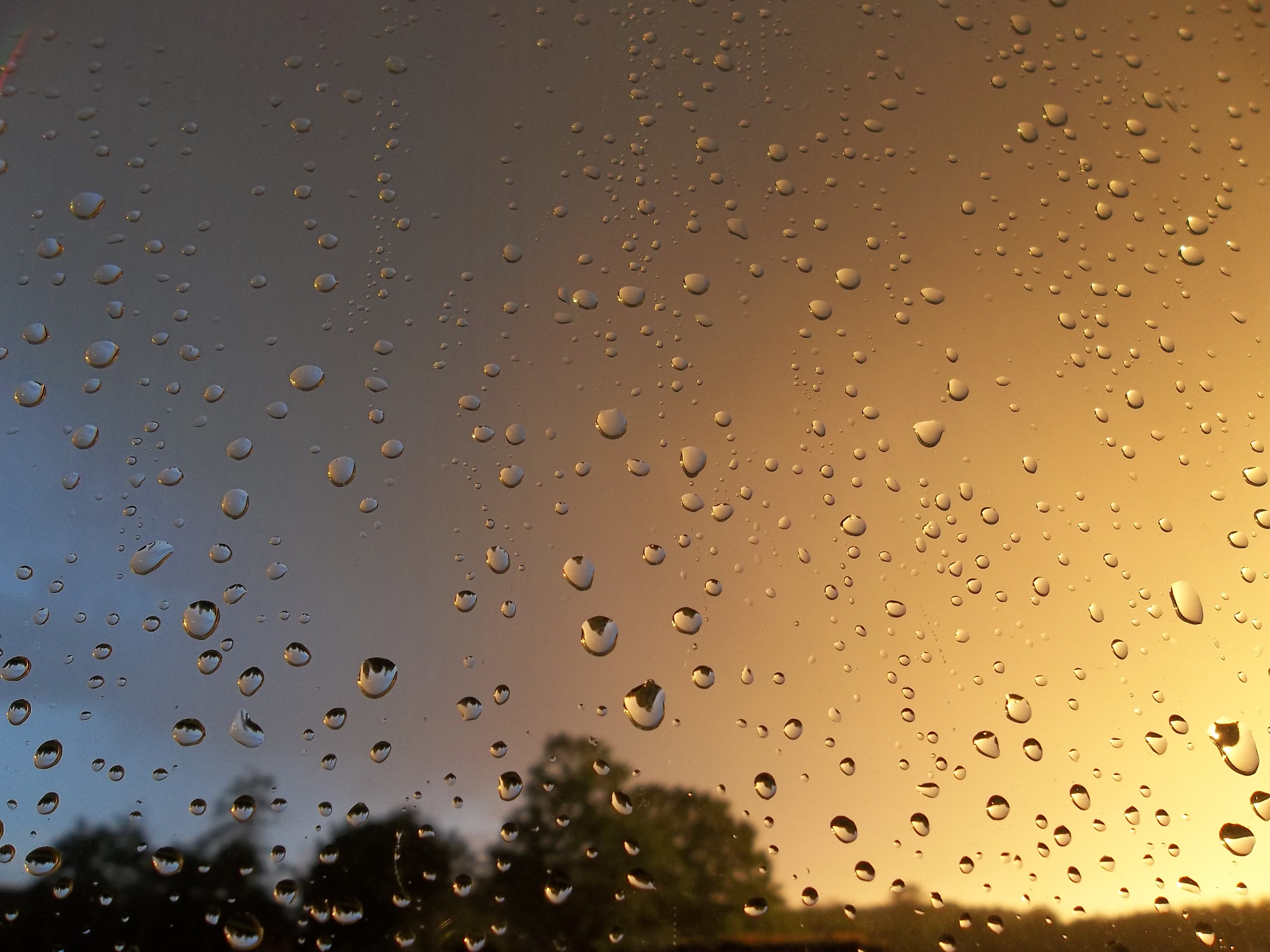 gotas de agua en un vidrio por la lluvia y al fondo nubes en el cielo y luz de sol