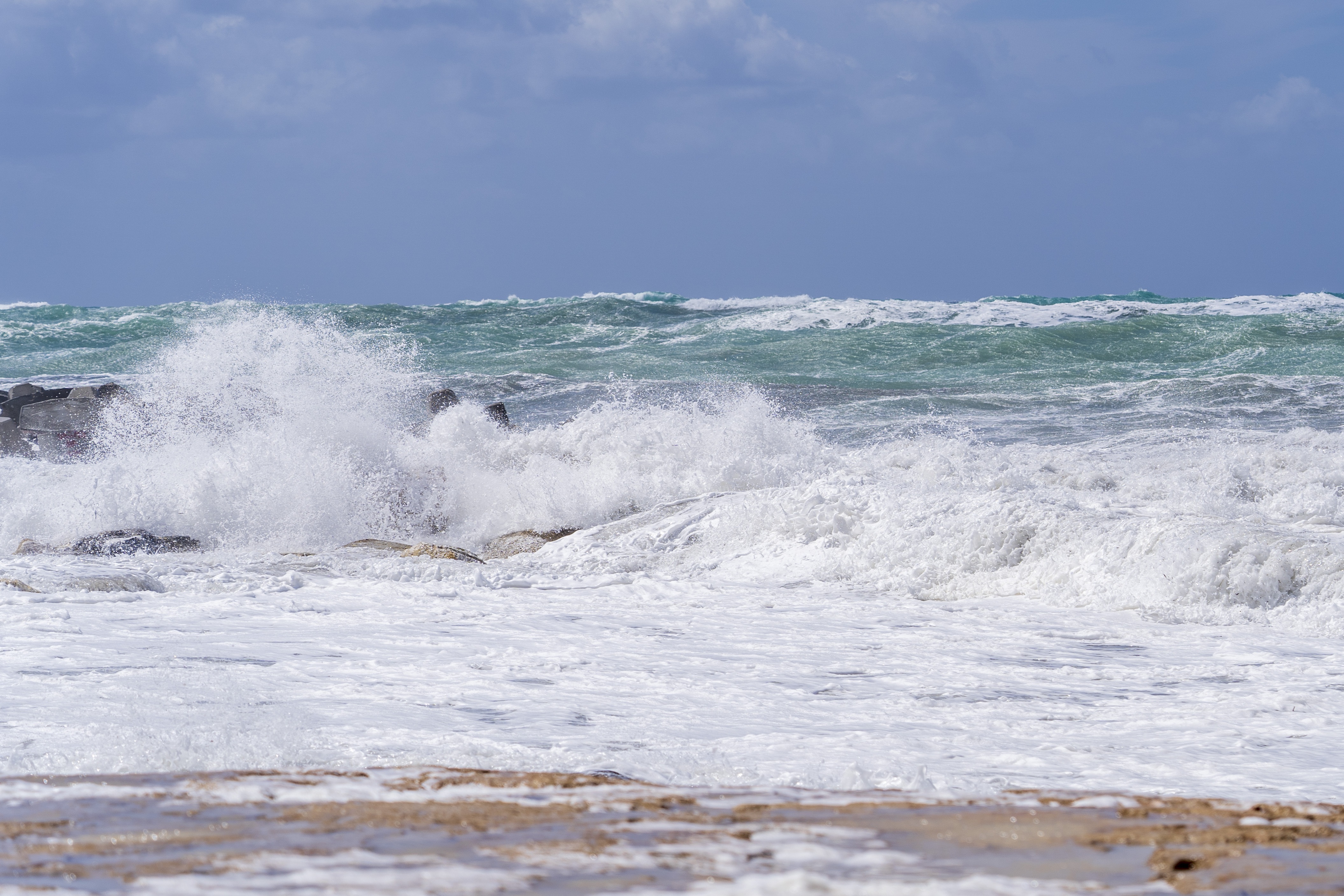 Olas fuertes golpeando en la costa en un mar azul y cielo nublado