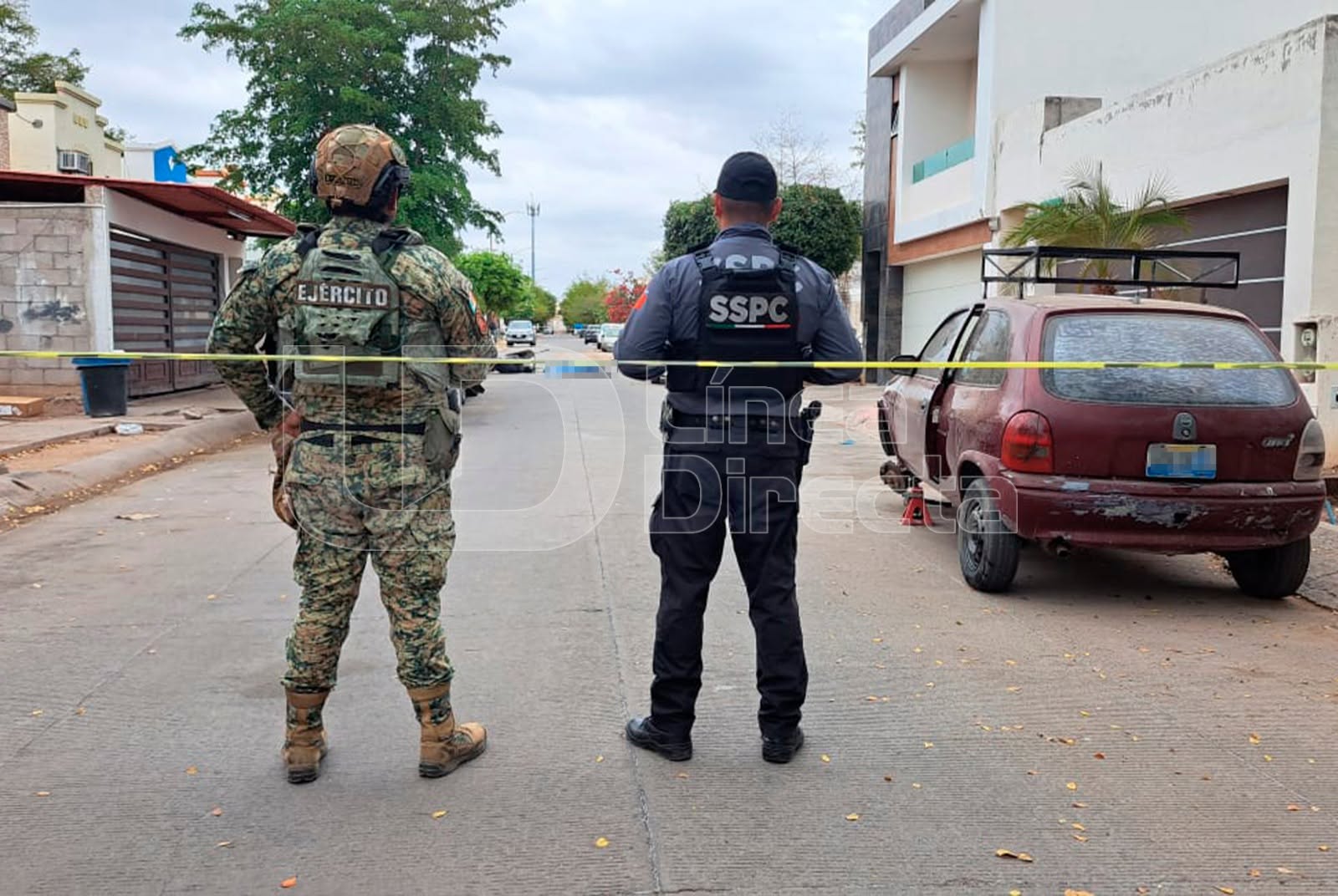 Elementos policacos de espaldas en una calle con una cinta de precaución
