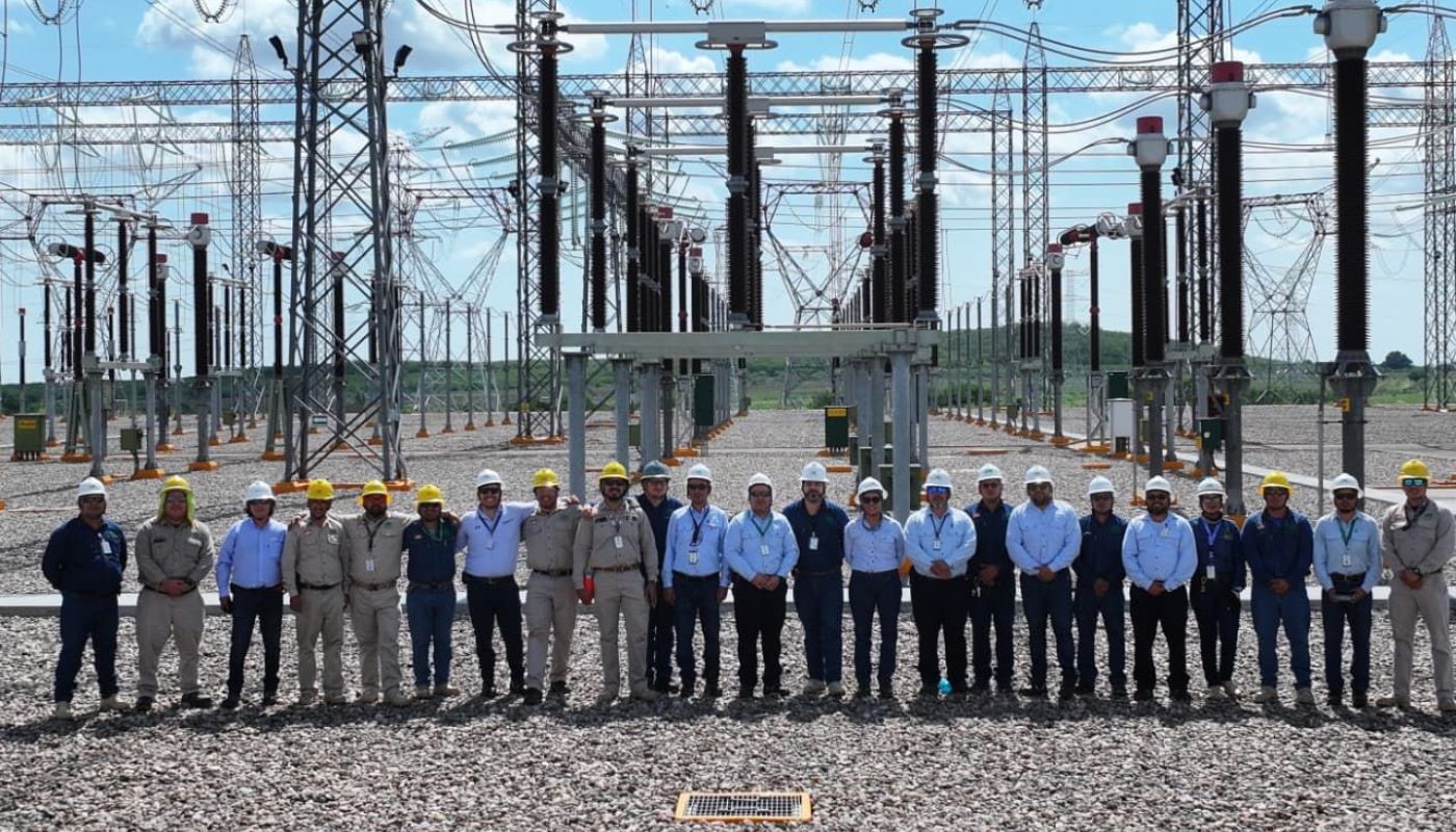 Personas con cascos viendo hacia el frente y al fondo una estación de energía eléctrica