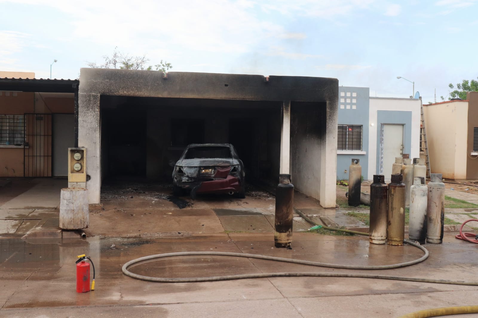 Chochera de una casa con un carro quemado y tanques de gas