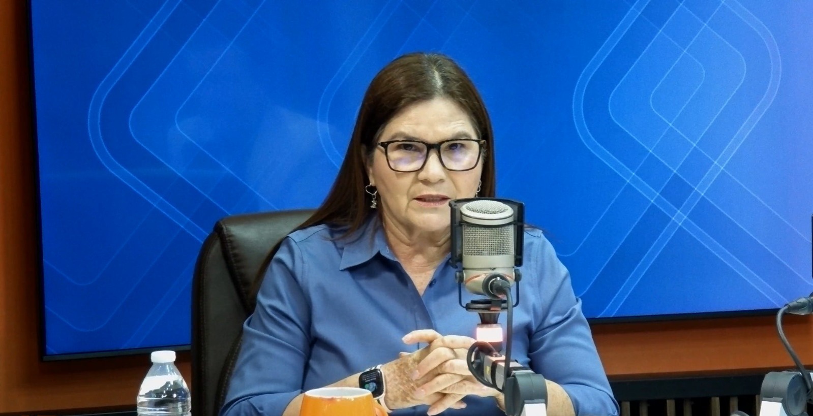 Imelda Castro con un micrófono frente a ella con fondo azul